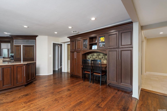 kitchen featuring paneled built in refrigerator, light stone counters, dark brown cabinetry, and dark wood-type flooring