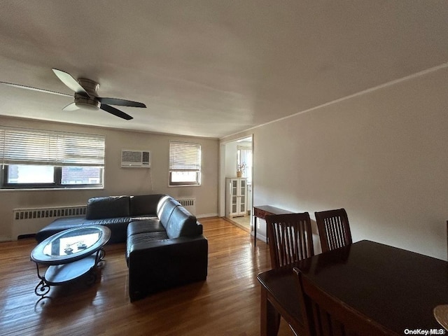 living room with a wall mounted air conditioner, ceiling fan, wood-type flooring, and radiator