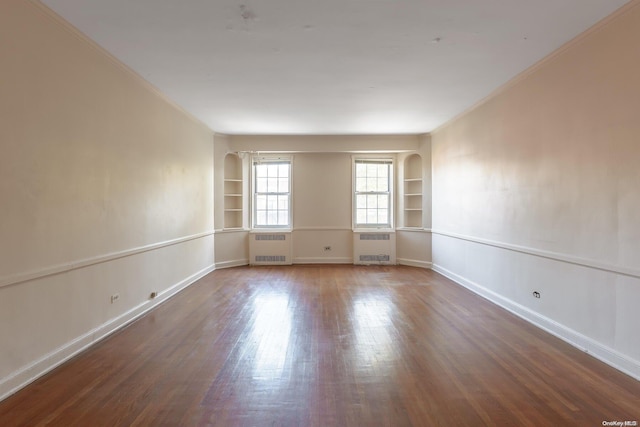 empty room with dark hardwood / wood-style flooring, built in features, ornamental molding, and radiator