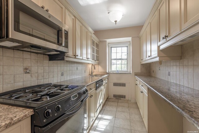 kitchen with cream cabinets, decorative backsplash, light tile patterned flooring, radiator heating unit, and black range with gas cooktop