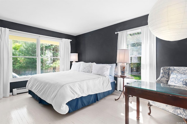 bedroom with light hardwood / wood-style floors, baseboard heating, and multiple windows