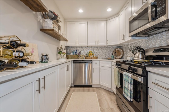 kitchen with backsplash, light hardwood / wood-style flooring, white cabinets, and appliances with stainless steel finishes