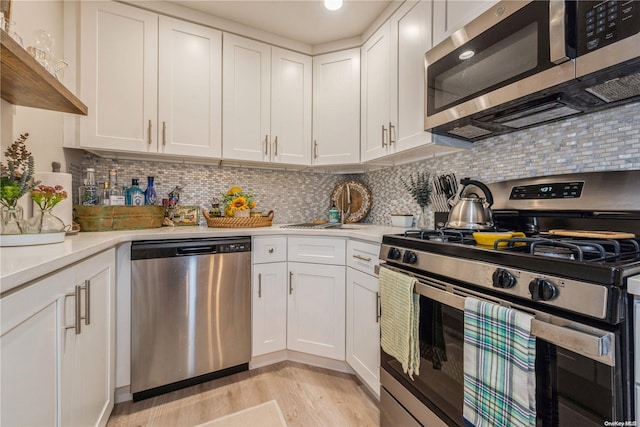 kitchen featuring tasteful backsplash, stainless steel appliances, sink, white cabinets, and light hardwood / wood-style floors