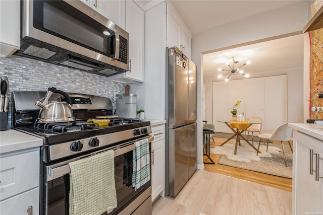 kitchen featuring decorative backsplash, light wood-type flooring, stainless steel appliances, a chandelier, and white cabinetry