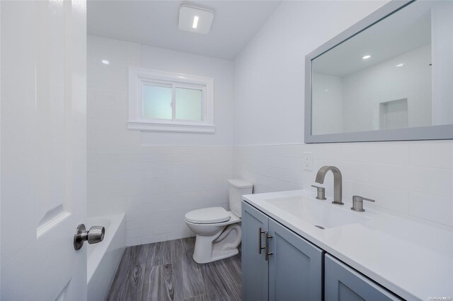 bathroom featuring wood-type flooring, vanity, toilet, and tile walls