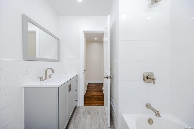 bathroom featuring vanity, wood-type flooring, tiled shower / bath combo, and tile walls