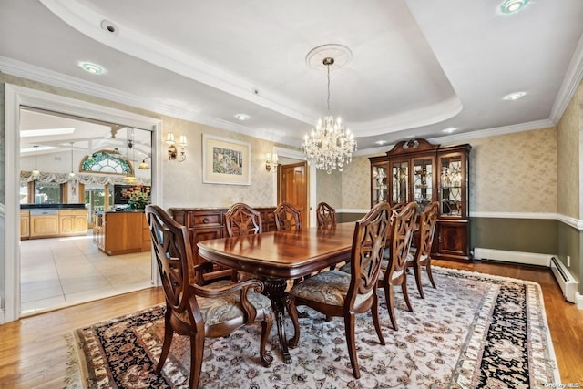 dining space featuring ornamental molding, a tray ceiling, baseboard heating, a notable chandelier, and light hardwood / wood-style floors