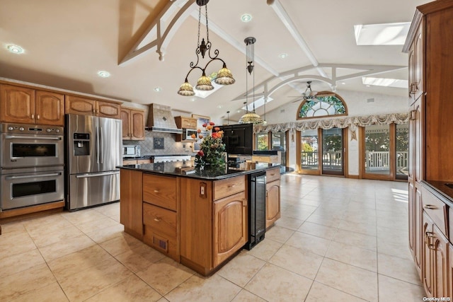 kitchen with ceiling fan, wall chimney exhaust hood, stainless steel appliances, lofted ceiling with skylight, and dark stone counters