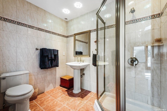 bathroom with a shower with door, sink, tile walls, tile patterned flooring, and toilet