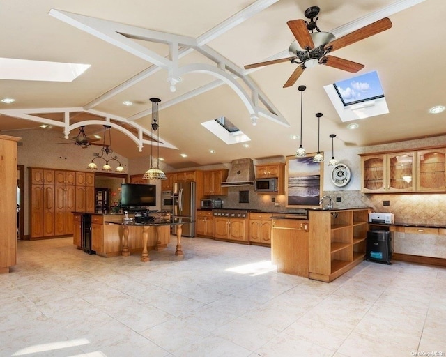 kitchen featuring a skylight, ceiling fan, stainless steel appliances, wall chimney range hood, and decorative light fixtures