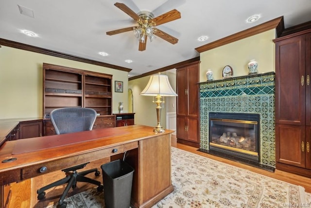 home office featuring a tiled fireplace, crown molding, ceiling fan, and light wood-type flooring