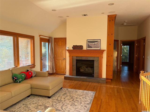 living room featuring a tile fireplace, light hardwood / wood-style floors, and vaulted ceiling