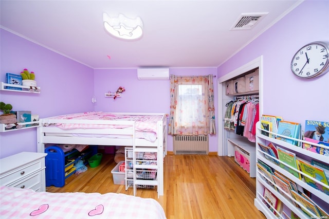 bedroom with ornamental molding, a wall mounted AC, radiator heating unit, light hardwood / wood-style floors, and a closet