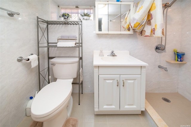 bathroom with a tile shower, tile patterned flooring, toilet, vanity, and tile walls