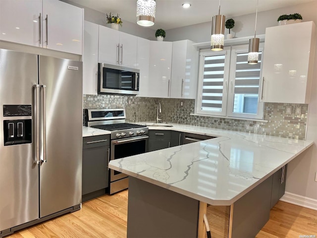 kitchen featuring white cabinets, appliances with stainless steel finishes, decorative light fixtures, light stone counters, and kitchen peninsula