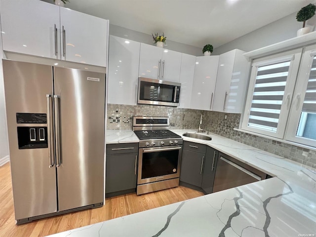 kitchen featuring white cabinetry, stainless steel appliances, light stone countertops, and sink