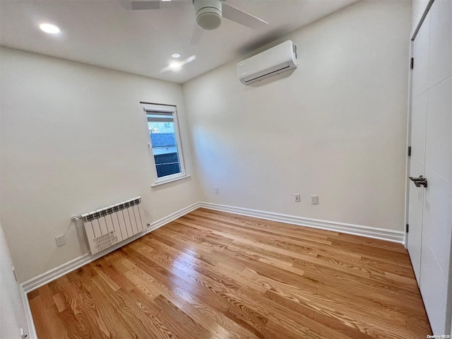 unfurnished room featuring ceiling fan, radiator, a wall mounted air conditioner, and light hardwood / wood-style floors