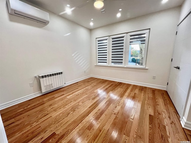 unfurnished room featuring an AC wall unit, radiator heating unit, and light hardwood / wood-style flooring