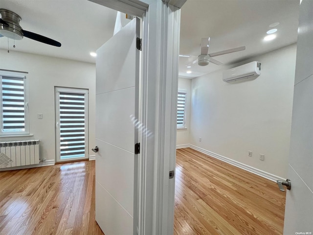 hallway with radiator heating unit, a wall unit AC, and light hardwood / wood-style flooring