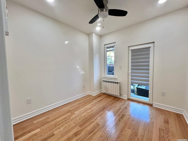 unfurnished room with ceiling fan, radiator heating unit, and light wood-type flooring