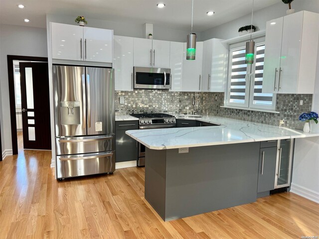 kitchen with stainless steel appliances, kitchen peninsula, white cabinets, and decorative light fixtures