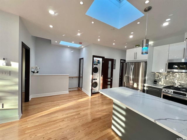 kitchen featuring appliances with stainless steel finishes, a skylight, white cabinets, hanging light fixtures, and stacked washer and dryer