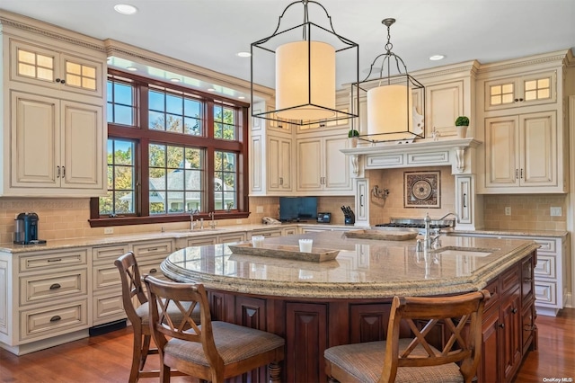 kitchen featuring a breakfast bar area, a kitchen island with sink, pendant lighting, and cream cabinetry