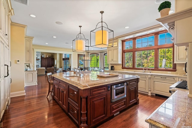 kitchen with a kitchen island with sink, sink, light stone countertops, decorative light fixtures, and stainless steel appliances