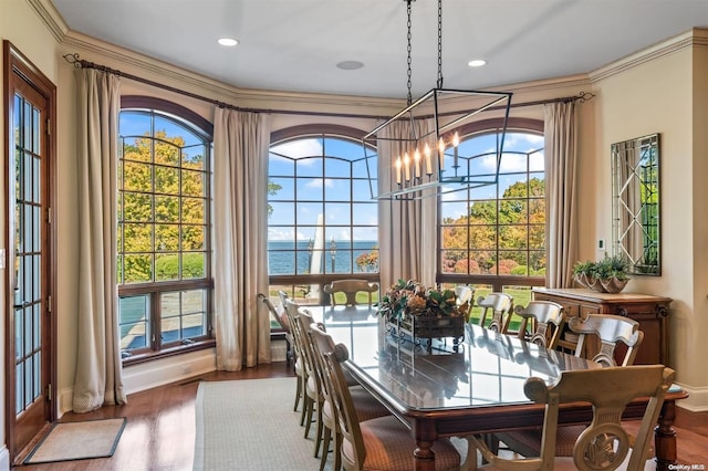 dining room with a chandelier, hardwood / wood-style floors, a water view, and crown molding