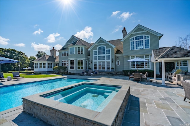 rear view of property featuring a swimming pool with hot tub, a patio, and area for grilling