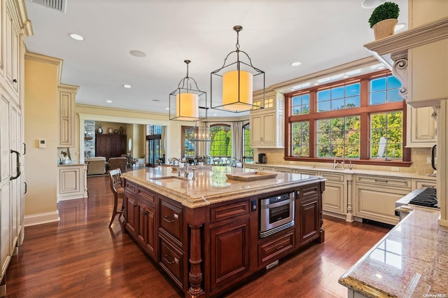 kitchen with a sink, cream cabinets, light stone countertops, and a center island with sink