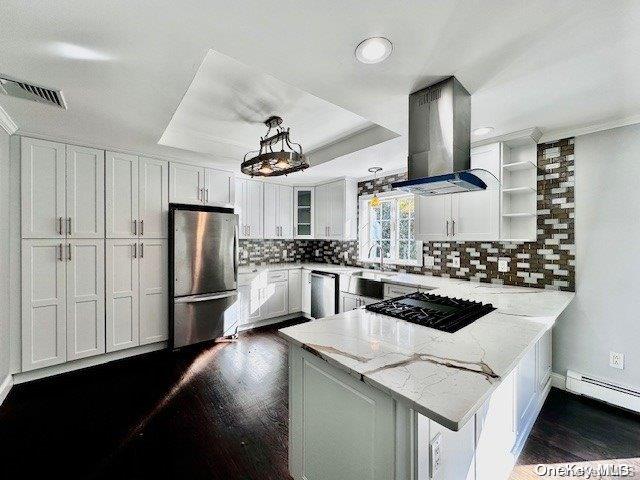 kitchen with pendant lighting, wall chimney range hood, kitchen peninsula, appliances with stainless steel finishes, and white cabinetry