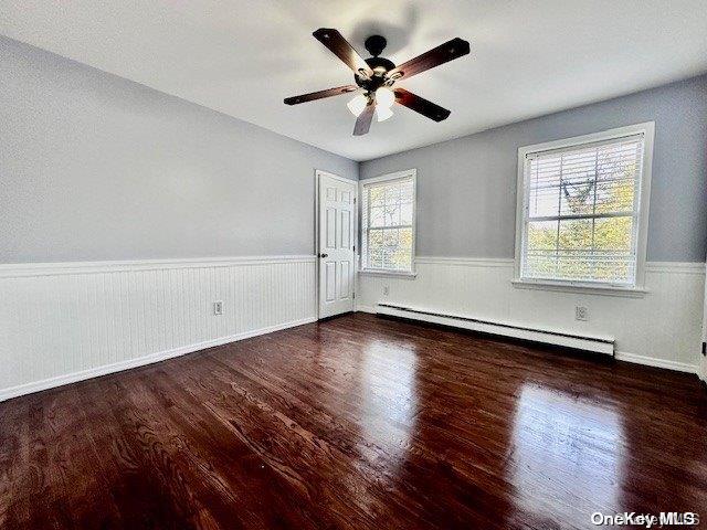 empty room featuring baseboard heating, ceiling fan, plenty of natural light, and dark wood-type flooring