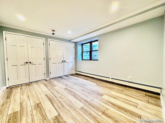 unfurnished bedroom featuring a textured ceiling, light hardwood / wood-style flooring, two closets, and a baseboard heating unit