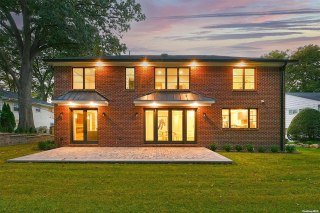 back house at dusk featuring a patio area, a yard, and french doors