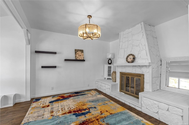 living room featuring an inviting chandelier, a stone fireplace, and dark wood-type flooring