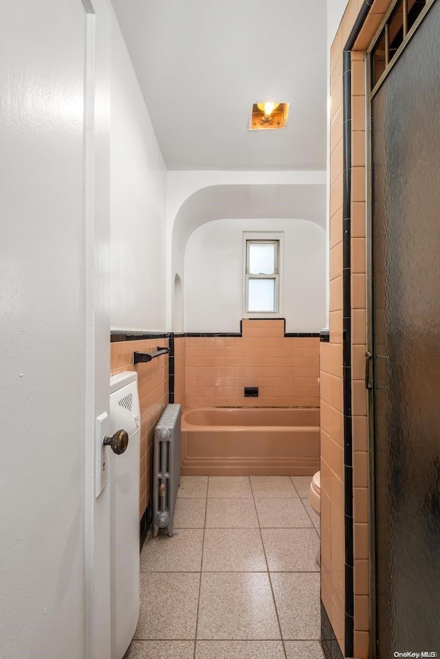 bathroom with radiator, a washtub, tile walls, and toilet