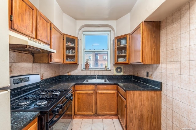 kitchen featuring sink, black range with gas cooktop, dark stone counters, decorative backsplash, and light tile patterned floors