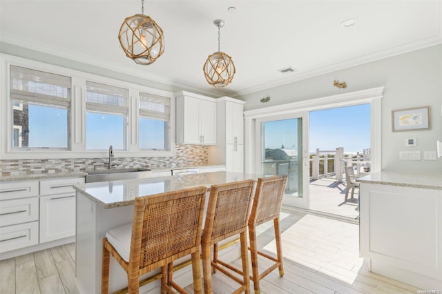 kitchen with a kitchen island, white cabinetry, hanging light fixtures, and ornamental molding