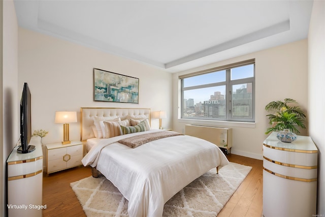 bedroom featuring radiator heating unit, a tray ceiling, and light hardwood / wood-style flooring