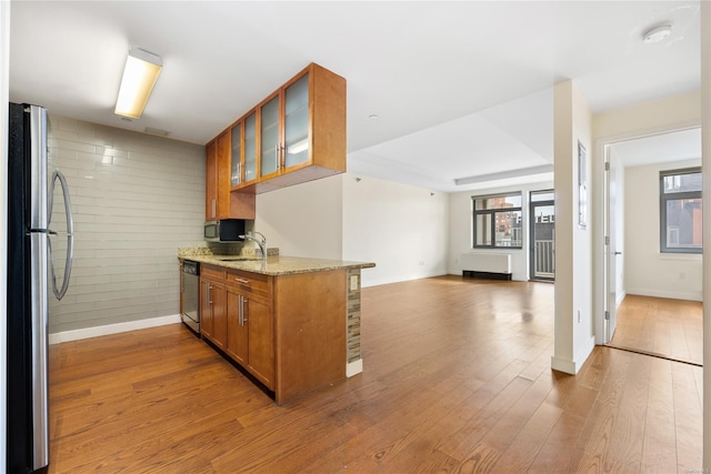 kitchen featuring sink, hardwood / wood-style floors, stainless steel appliances, light stone counters, and kitchen peninsula