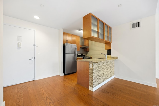 kitchen with sink, stainless steel appliances, tasteful backsplash, kitchen peninsula, and light wood-type flooring