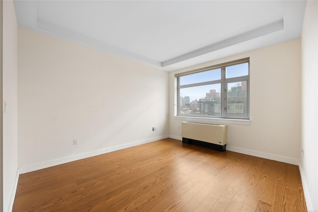 unfurnished room featuring radiator, a raised ceiling, and light wood-type flooring