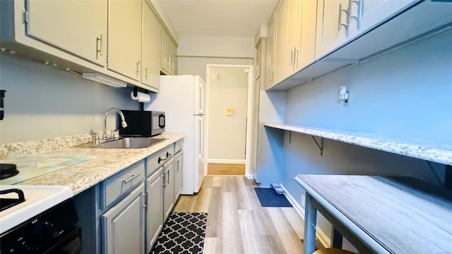 kitchen with light stone countertops, sink, stove, white fridge, and light hardwood / wood-style floors