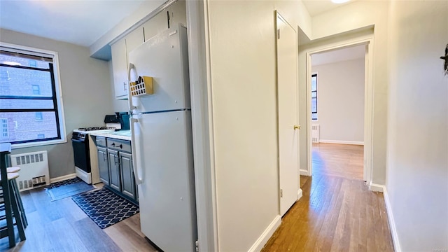 kitchen featuring gray cabinetry, light wood-type flooring, white appliances, and radiator