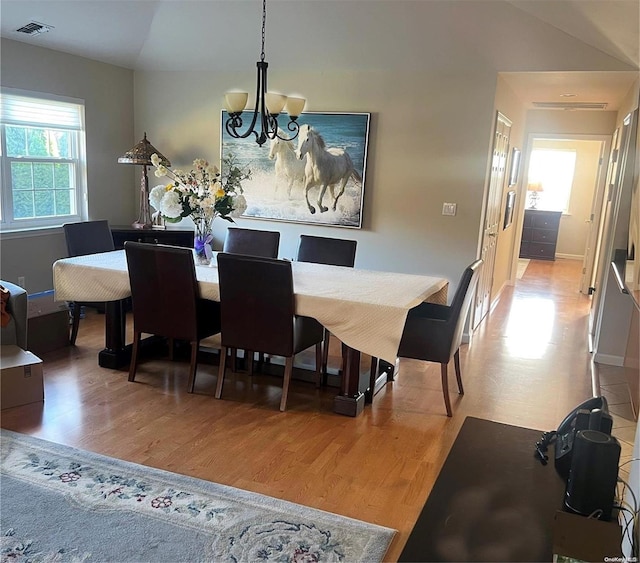 dining room featuring hardwood / wood-style floors, vaulted ceiling, and an inviting chandelier