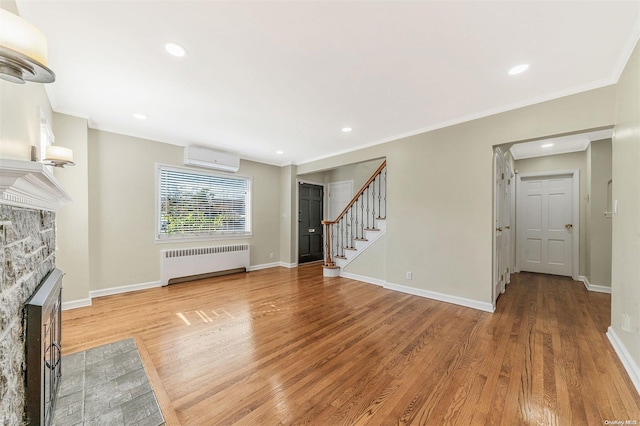 unfurnished living room with crown molding, radiator heating unit, a fireplace, a wall mounted AC, and wood-type flooring