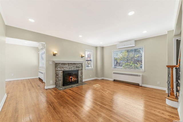 unfurnished living room featuring radiator heating unit, light hardwood / wood-style floors, a stone fireplace, and a wall mounted AC