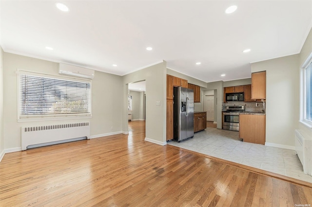 kitchen featuring radiator, a wall mounted air conditioner, light hardwood / wood-style floors, appliances with stainless steel finishes, and ornamental molding