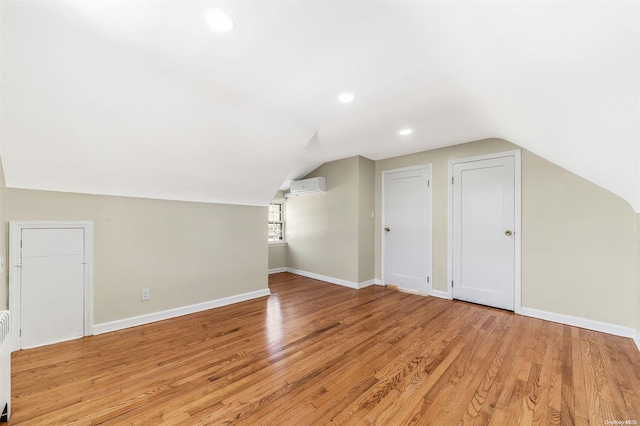 bonus room featuring an AC wall unit, vaulted ceiling, and light wood-type flooring